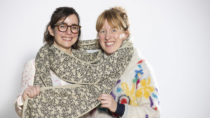 Two women wrapped in a long handmade scarf