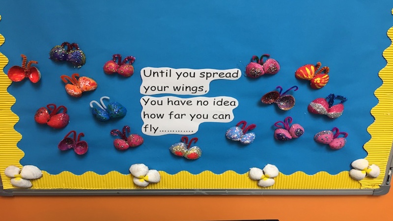 Butterfly art made by children at Balivanich Primary School. There are a number of butterflies and the words 'until you spread your wings you have no idea how far you can fly'. The butterflies are on a blue paper background with a yellow border and decorated with shells.