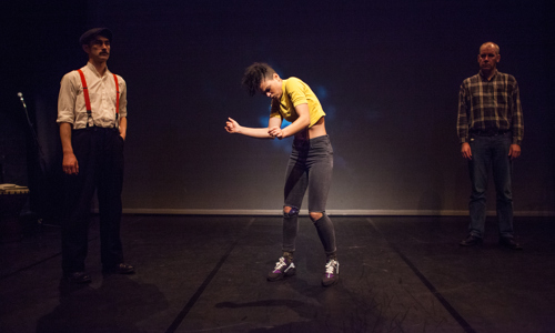 Three performers on stage during Gaelic Arts. The performer in the middle dances as the others look on