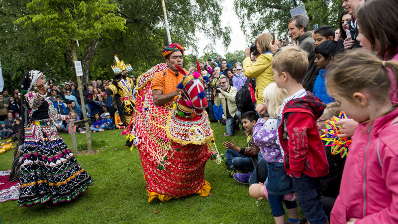 Children watching brightly coloured performers at Glasgow Mela with other members of the crowd taking photographs.