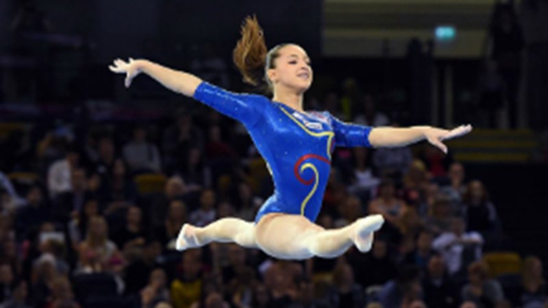 Female gymnast leaping wearing a blue leotard. 