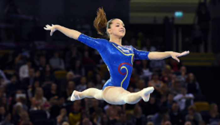 Female gymnast leaping wearing a blue leotard. 