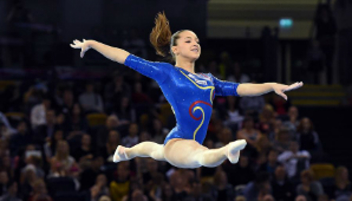 Female gymnast leaping wearing a blue leotard.