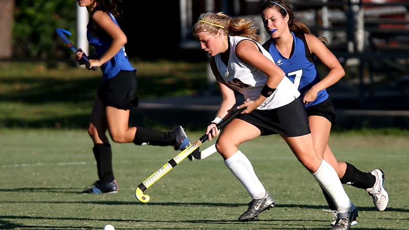 A group of young women playing  filed hockey outside on a sunny day