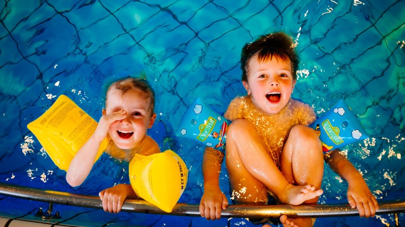 Two young boys play in the pool with armbands on