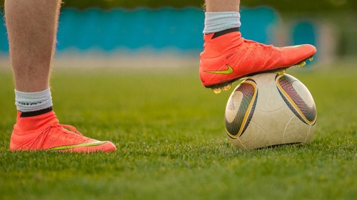 footballer with foot on a football on grass pitch 