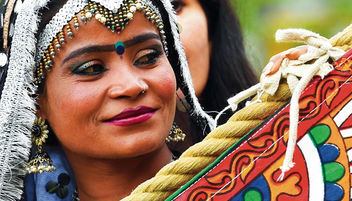 A person with a headress and traditional South East Asian dress smiling and holding a multicoloured banner
