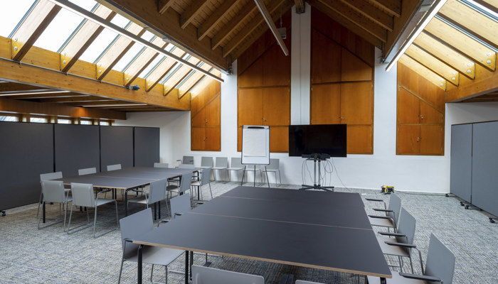 large meeting space with two large tables with chairs round them. the room has windows up high with wooden panelling across the roof