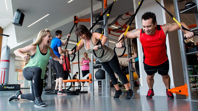 man and woman using gym equipment with personal trainer 