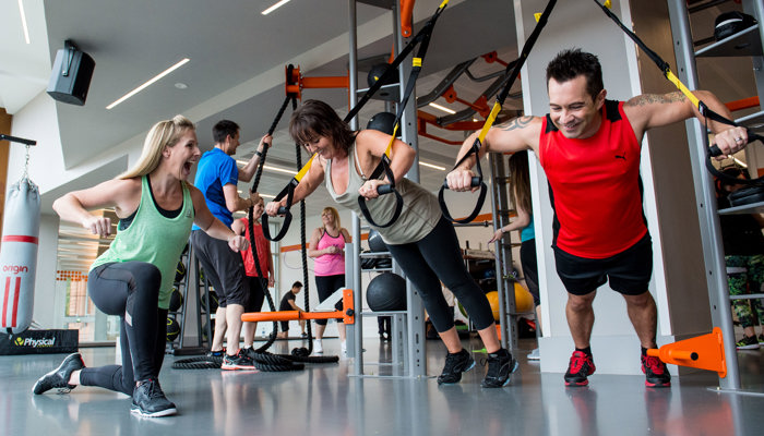 man and woman using gym equipment with personal trainer 