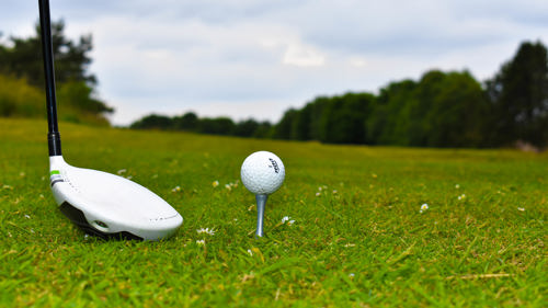 Golf ball on tee beside golf club 