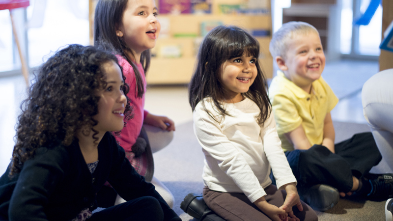 Group of children in a library smiling and listening to someone reading a story