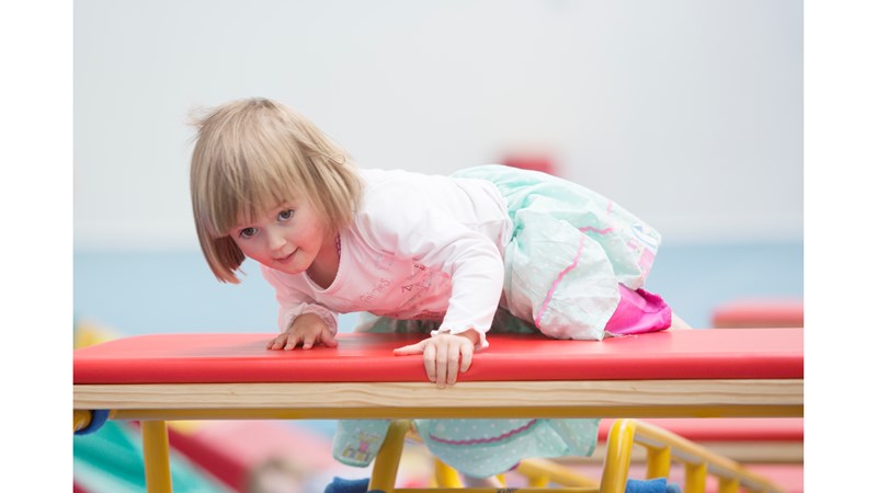 Little girl climbing up on gymnastic equipment 