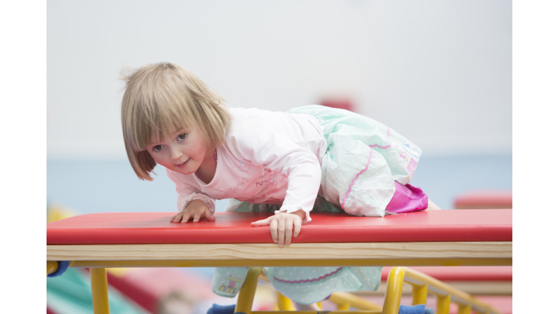 Little girl climbing up on gymnastic equipment 