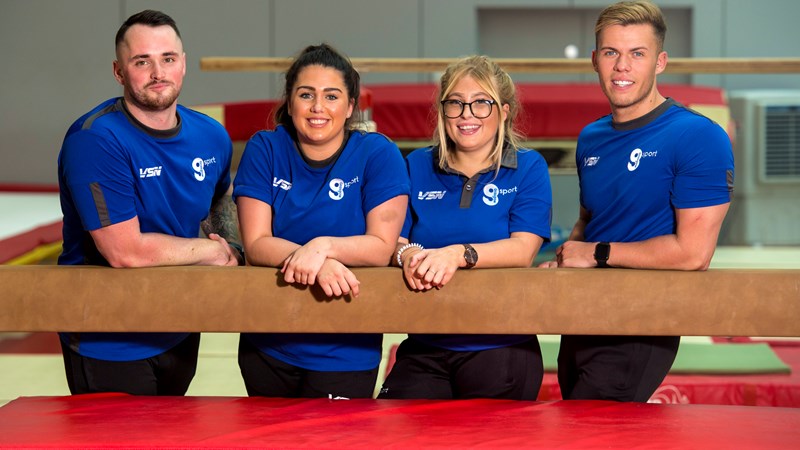 4 instructors wearing blue uniforms leaning on balance bar smiling. 