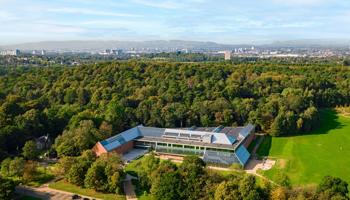 Aerial shot of the refurbished Burrell Collection. The modern glass structure is surrounding by green space and lots of trees.