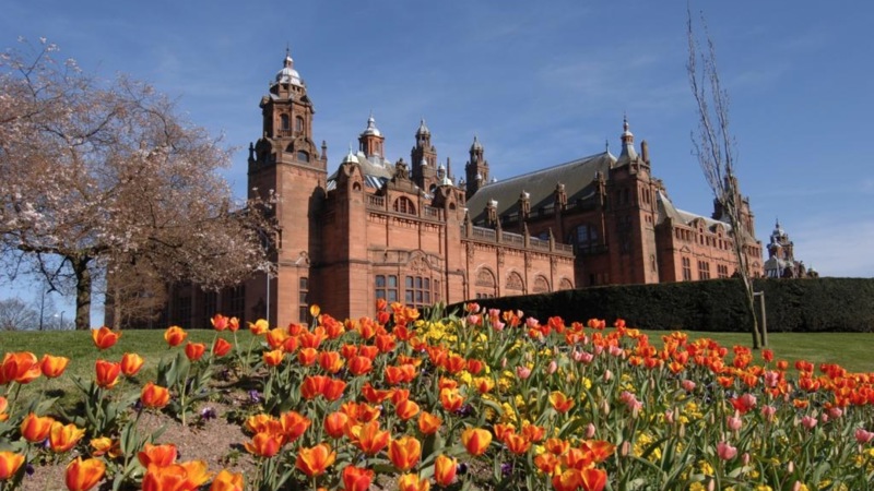 Glasgow's Kelvingrove Art Gallery and Museum on a spring day. There are red and yellow tulips in the foreground, as well as a tree with no leaves.