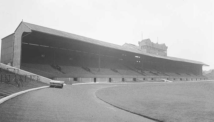 A black and white photo of inside an empty football stadium showing the grounds and seating.