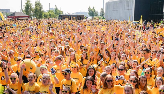 a crowd of people dressed in yellow looking happy and cheering as they set off on a charity walk together 