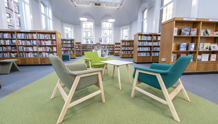 Three colourful chairs are sat around a small wooden table in Partick, with rows of full bookcases visible in the background.