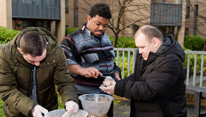 Three people in an outdoor setting mixing food in bowls