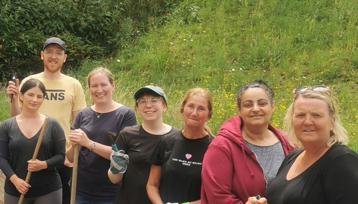 Group of people outside, standing looking at camera with gardening tools. 