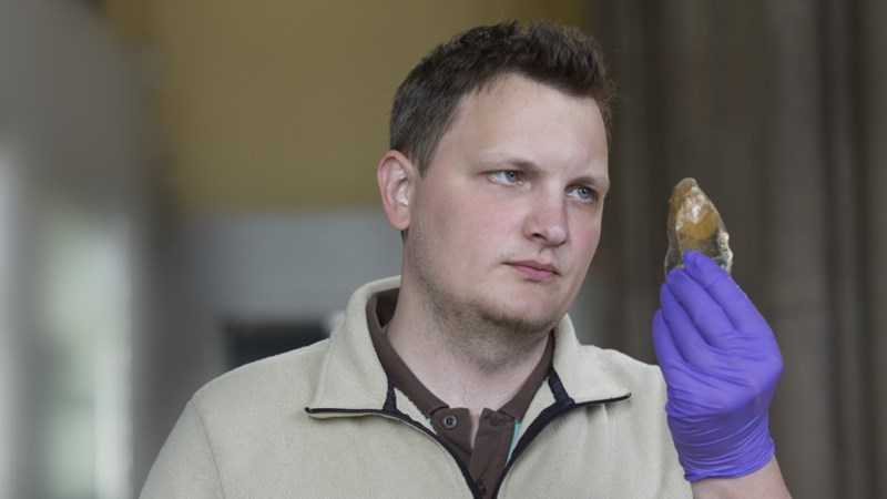 A man is wearing protective gloves and holding up an object from The Hunterian collections for closer inspection