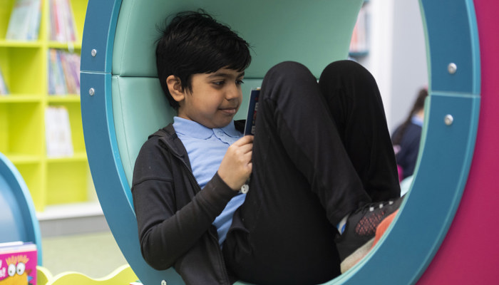 Primary aged child sitting reading a book, in a reading tunnel in the children's section of Woodside library