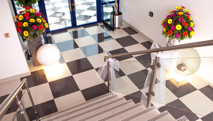 staircase with black and white checked flooring at the bottom. there are white ribbons attached to the the banister ready for a wedding. There are also two flowers arrangements at the door just beyond the bottom of the stairs