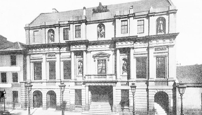 A black and white photo of a building with many architectural statues on it and lots of windows.