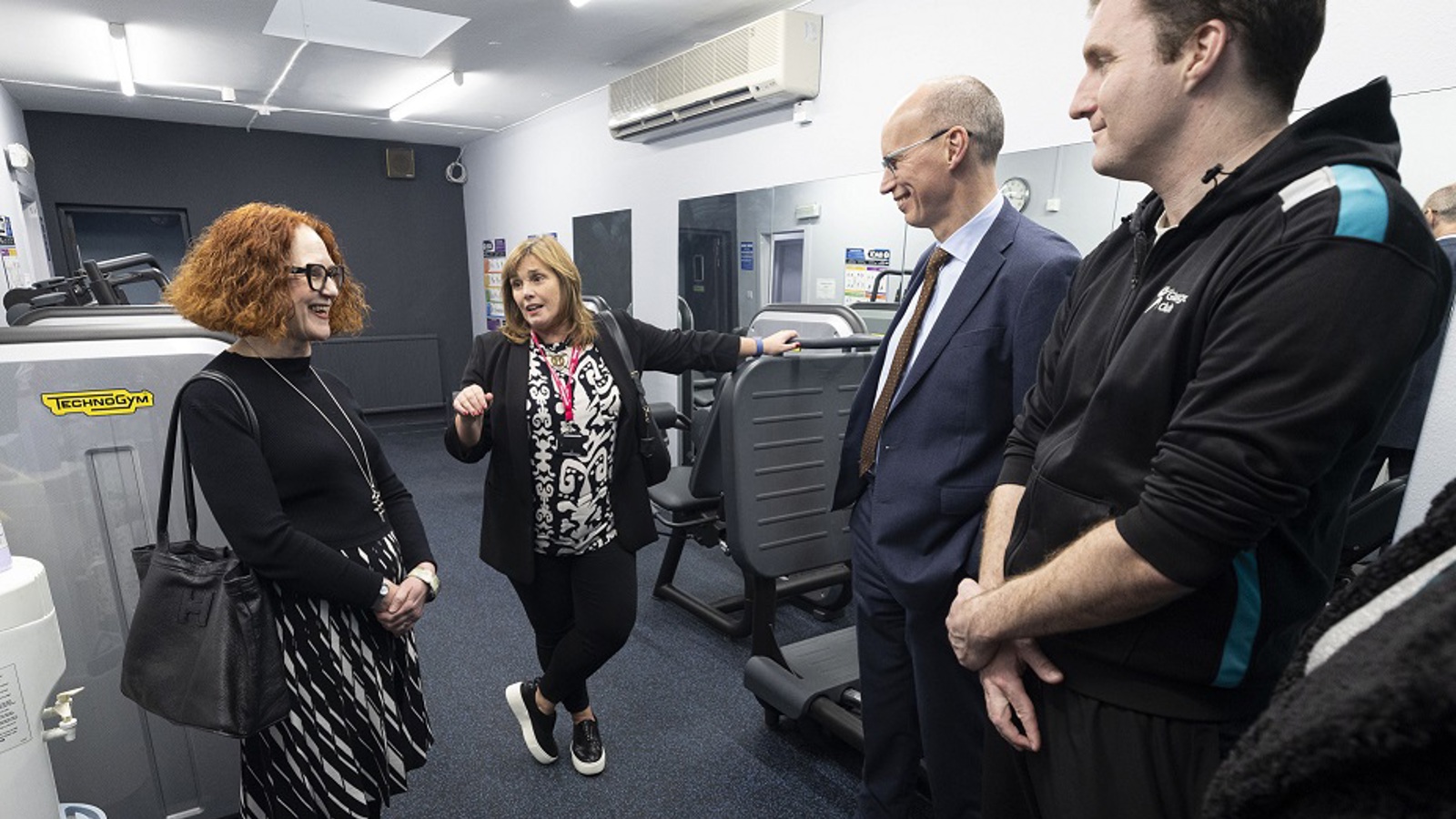 A group of four people gathered around new gym equipment in a new indoor gym space in a community centre