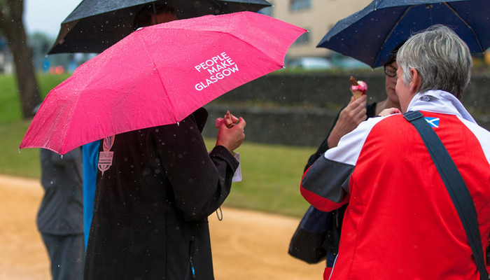 Four people gathered under four umbrellas, one of the umbrellas is pink and says People Make Glasgow.