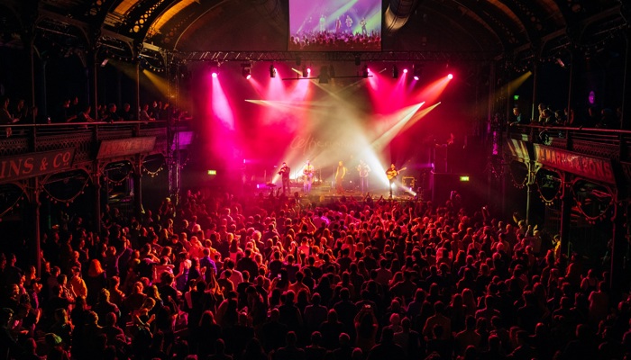 A large concert venue, packed with hundreds of revellers, dramatic light focused on a stage