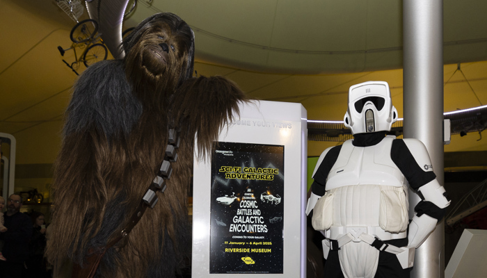 Characters stand next to a digital poster promoting a new science fiction exhibition at Glasgow's Riverside Museum