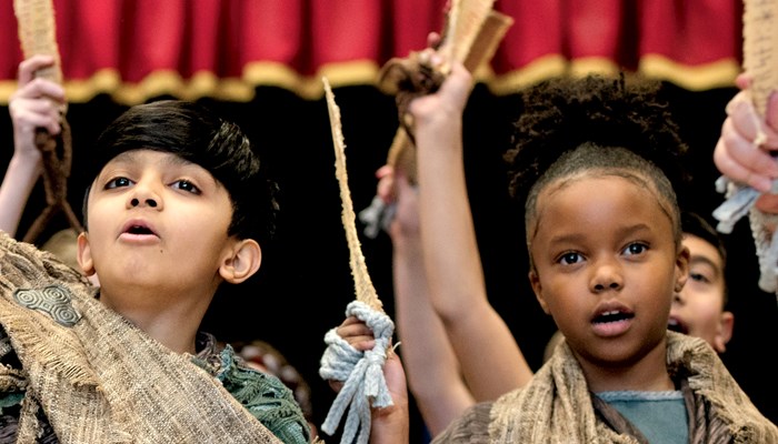 Two primary age children dressed in traditional Viking clothing are singing and looking at the camera during a workshop performance