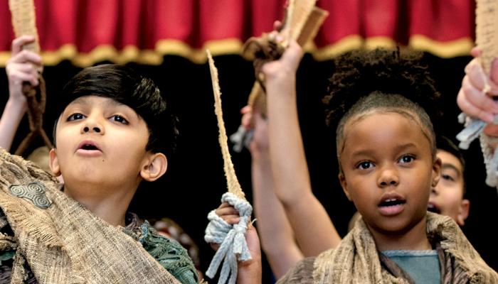 Two primary age children dressed in traditional Viking clothing are singing and looking at the camera during a workshop performance