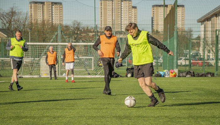 Footballers wearing orange and yellow bibs enjoy a game of walking football