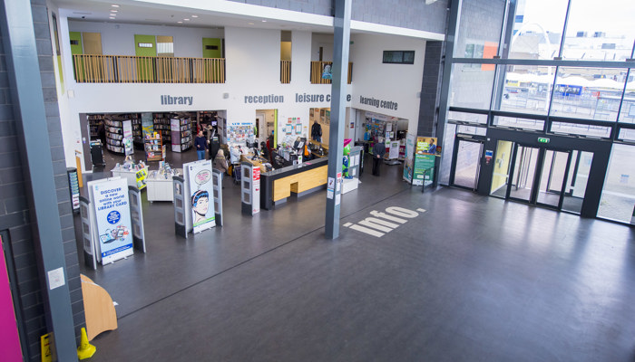 Large modern entrance to Pollok Library which has large windows, a grey floor with the word 'info' in white letters and a mezzanine