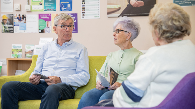 Three people sitting on chairs and sofa having a conversation