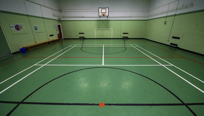 games hall which is marked out for different games. the floor is marked in green with white, black and red lines for the games. the walls are painted light green. there is a basketball net on the far wall