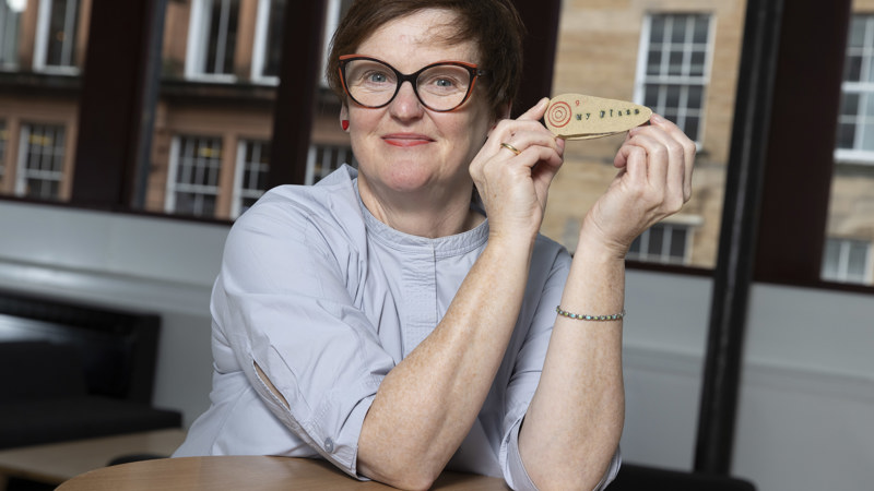 A smiling woman displays a small wooden artwork