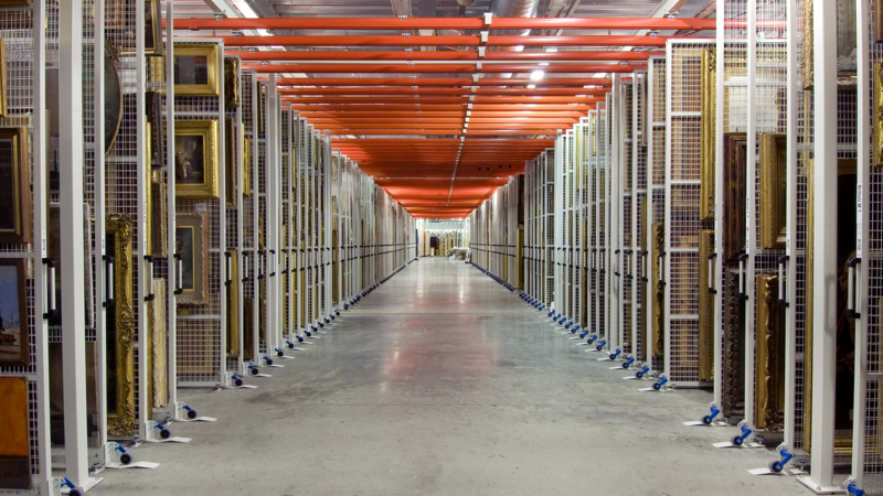 A view down a corridor in the vast painting store at Glasgow Museums Resource Centre with racks of paintings either side