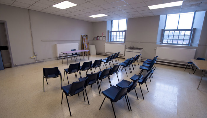 room with lots of blue chairs facing the front ready for a presentation. there are two large windows on far away wall