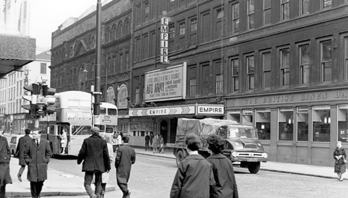 A black and white photo of a busy Glasgow street with pedestrians and cars on the road with buildings on either side including a theatre