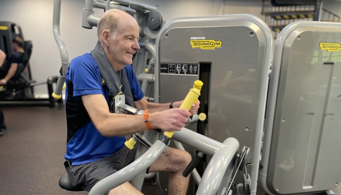 Glasgow Club member Raymond Ward using a low row back machine at Glasgow Club Tollcross gym. They have their arms out in front of them holding onto the handles of the machine.