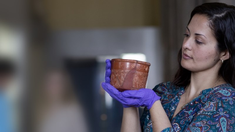 A woman holding up a piece of pottery from The Hunterian collections