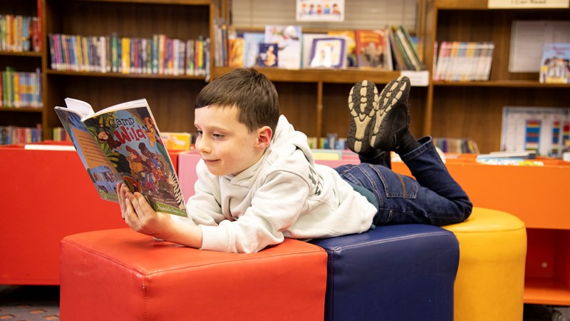 A young boy in a library reading a comic