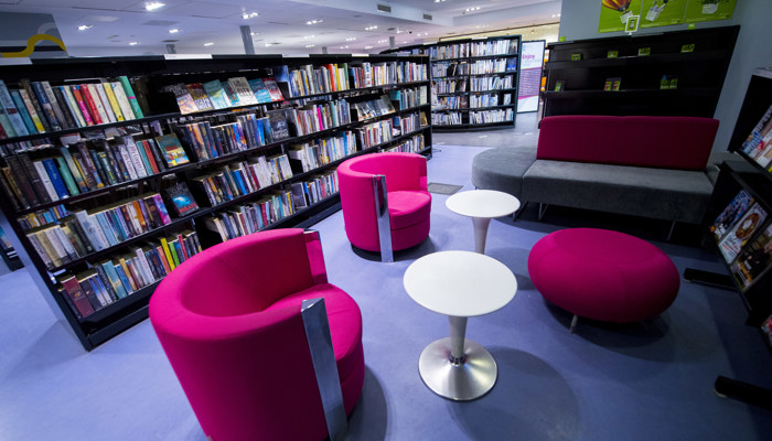 Black bookshelves with pink circular soft chairs on a purple carpet