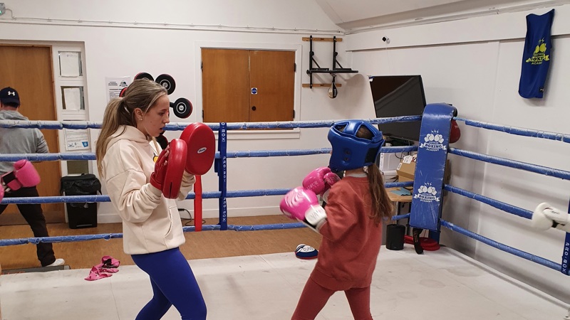 Volunteer holding pads while helping a child box