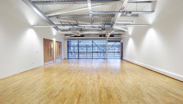 an empty rooms with windows at the end. The floor has a wooden effect and the walls are white